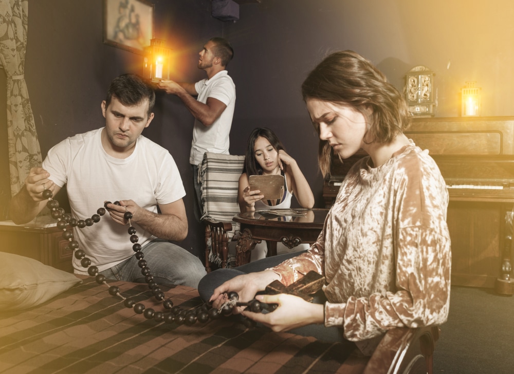 Group of young adults inspecting wooden rosary, trying to find solution of conundrum in escape room with antique furnitures