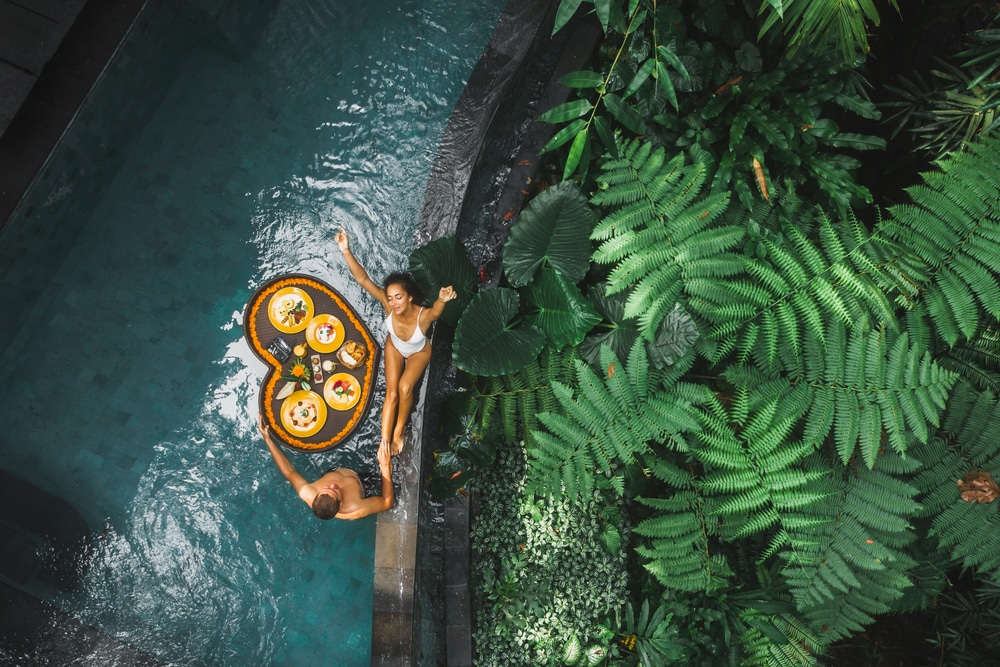 Travel happy couple in love eating floating breakfast in jungle swimming pool