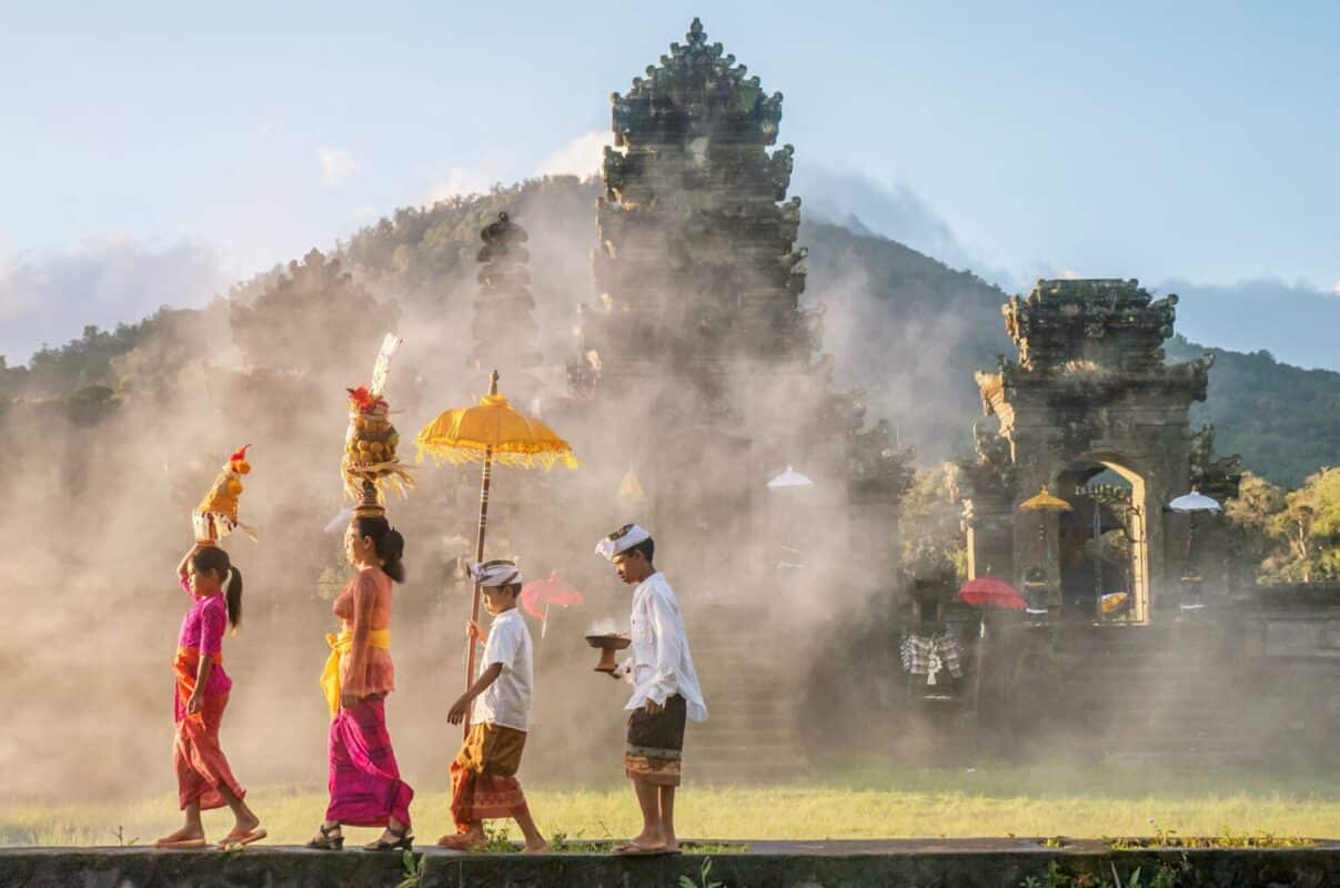 Traditional Balinese male and female ceremonial clothing and religious offerings, as a mother and children walk to a Hindu temple (pura).