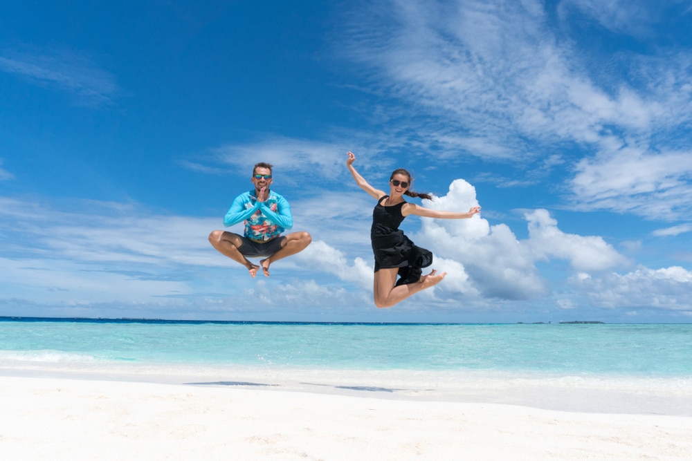 Man and woman jump on beach with transparent water of ocean in Maldives