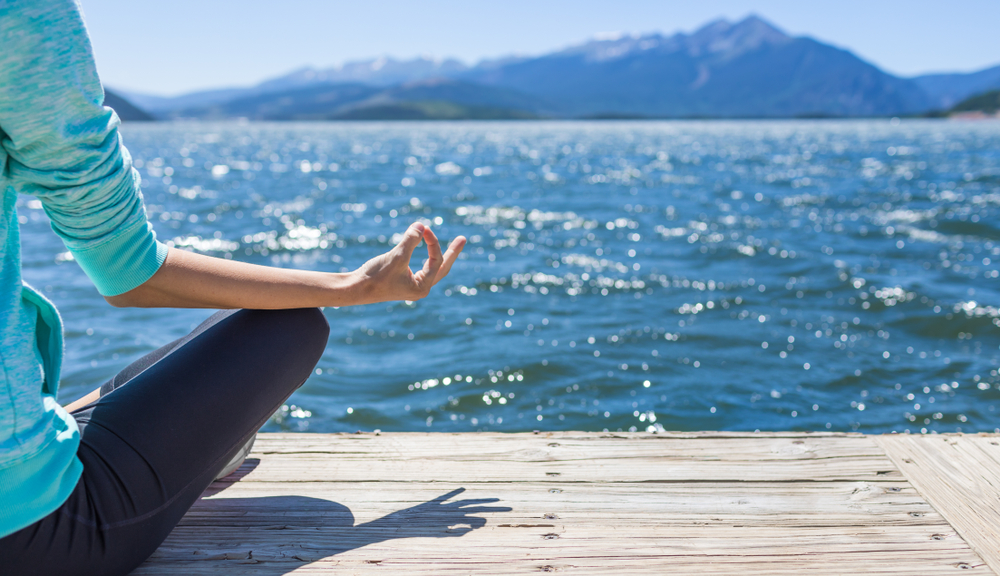 Female In Lotus Position Meditating Lake Side.