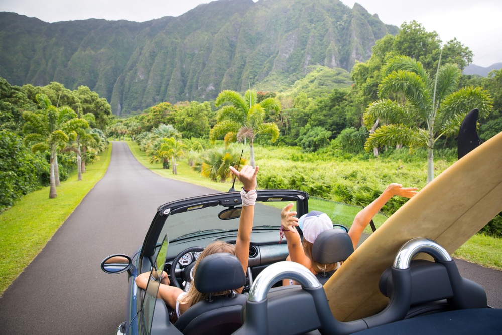 Road trip travel - girls driving car in freedom. Happy young girls cheering in convertible car on summer Hawaii vacations.