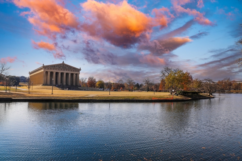 a gorgeous autumn landscape at Centennial Park with a still lake surrounded by autumn colored trees reflecting off the water and powerful clouds at sunset in Nashville Tennessee USA